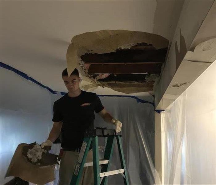 tech on a ladder removing water damaged ceiling sheetrock