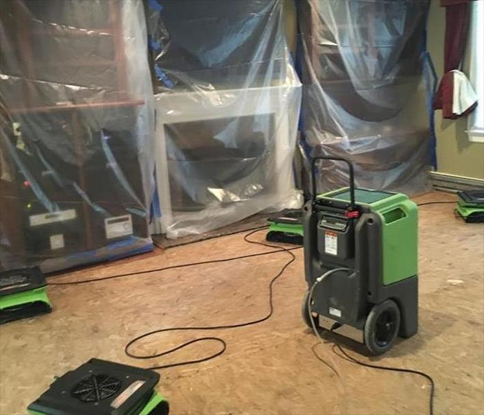 Furniture covered with plastic, with SERVPRO equipment on the floor. 